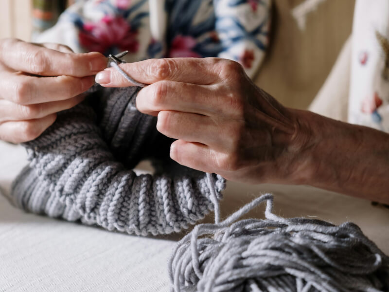 Close-up of old woman's hands knitting with grey yarn